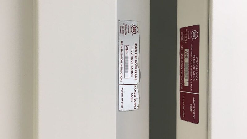 Certifieringsetiketter för brandklassade dörrar och dörrkarmar på ett hotell.