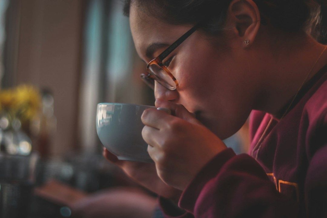 Person med glasögon dricker kaffe ur en ljus kopp under en paus