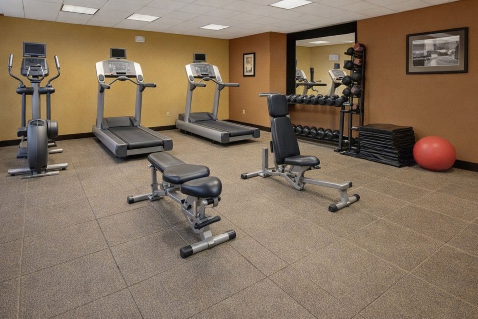 Ett litet hotellgym med löpband, träningsbänkar och hantlar.